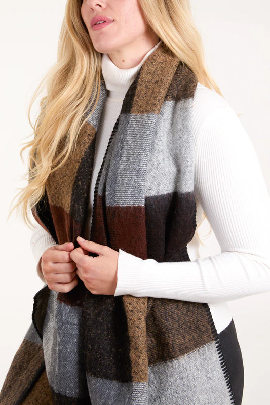 Woman wearing a white ribbed polo-neck jumper and a large colour-block scarf in shades of brown, grey, and black.