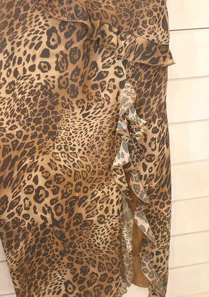 Brown and black leopard print fabric with a ruffled edge and side slit, this Leopard Long Dress in Size 12 is showcased against a light-coloured wooden background.