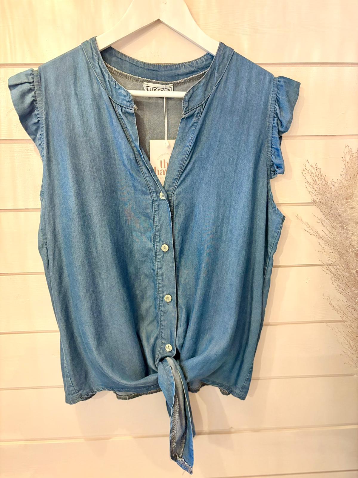 Sleeveless chambray button-up shirt featuring a front tie, made from eco-friendly vegan materials, shown on a white hanger against a light wooden background.
