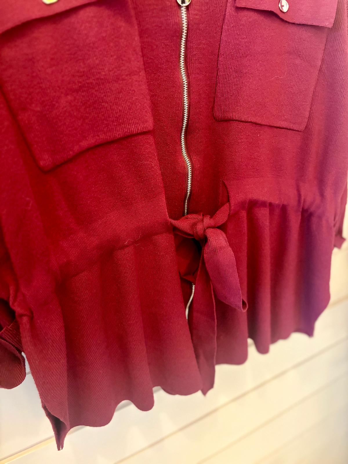 A close-up of a red garment featuring a zip, two front pockets, and a fabric tie at the waist.