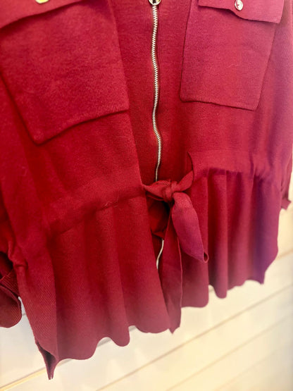 A close-up of a red garment featuring a zip, two front pockets, and a fabric tie at the waist.