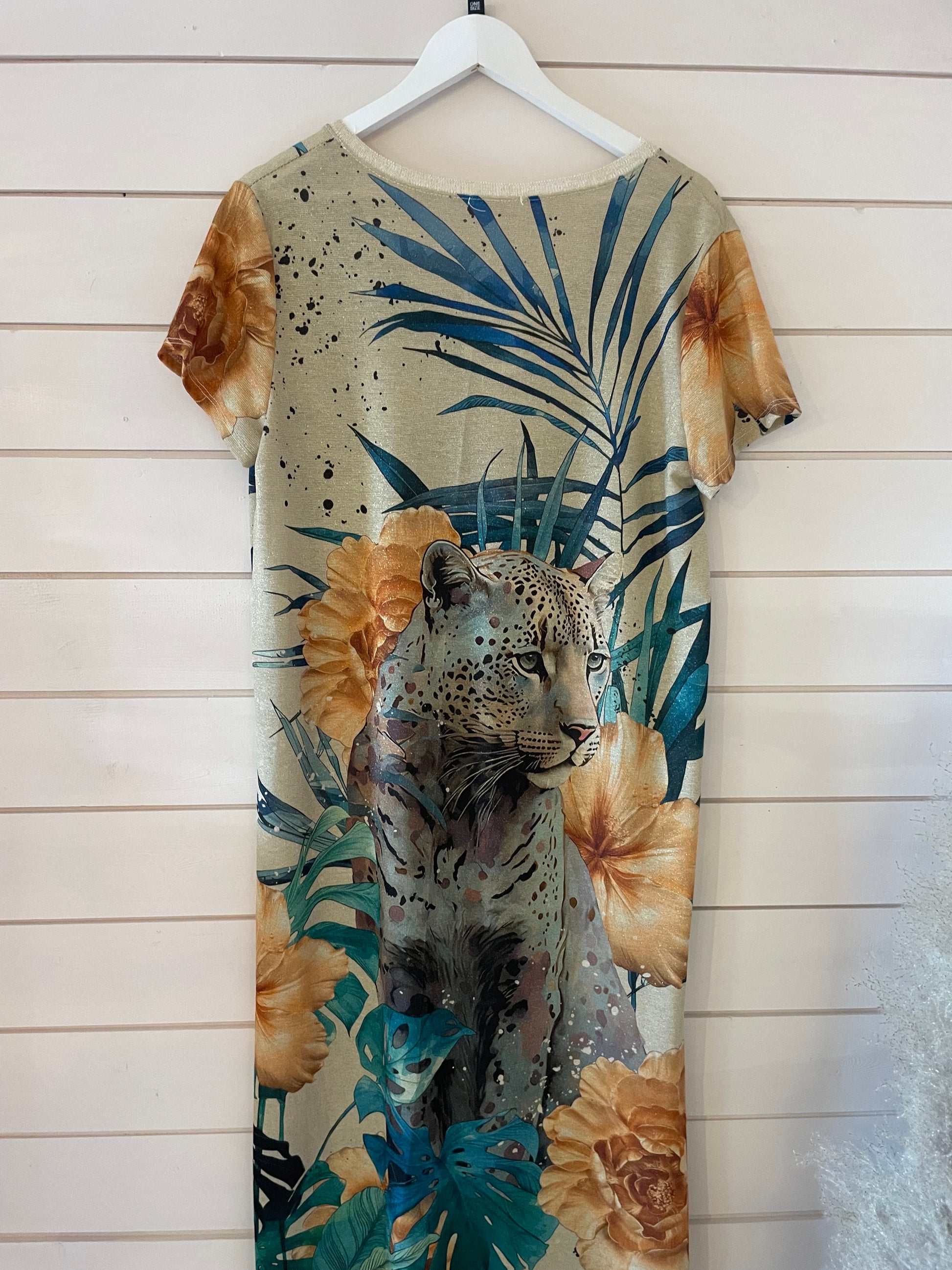 Short-sleeved evening dress featuring a large printed leopard surrounded by yellow flowers and green leaves, crafted from shimmering fabric and hanging on a white wooden wall.