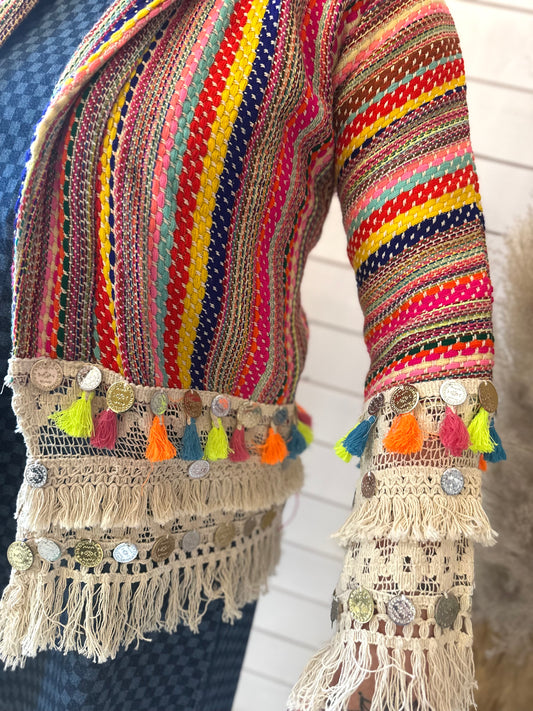 A person wearing a vibrant Boho Multi Stripe Jacket featuring multicoloured stripes, tassels, coins, and fringe detailing on the sleeves and hem—perfect for a bohemian festival look.