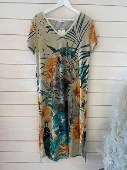Short-sleeved, V-neck evening dress featuring a bold leopard and tropical leaf pattern in beige, green, and brown hues, made from shimmering fabric and displayed on a white hanger against a wood-panelled wall.