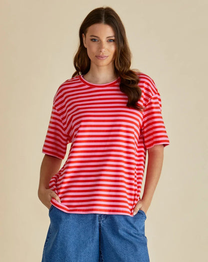 Woman wearing a loose-fitting, vegan-friendly red and white striped boxy tee and blue denim shorts, standing against a plain beige background.