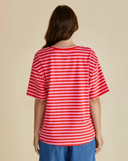 Person standing with their back to the camera, wearing a vegan-friendly red and white striped t-shirt and blue jeans against a plain beige background.