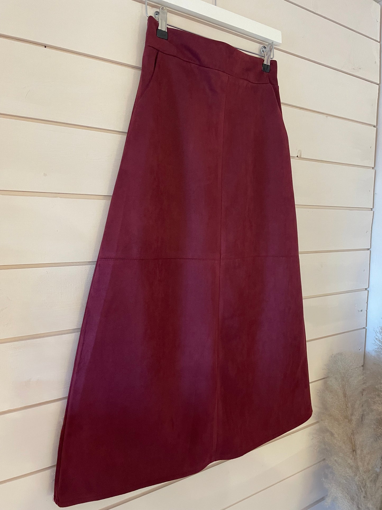A vegan-friendly burgundy A-line skirt hangs on a white hanger against a light wooden wall.