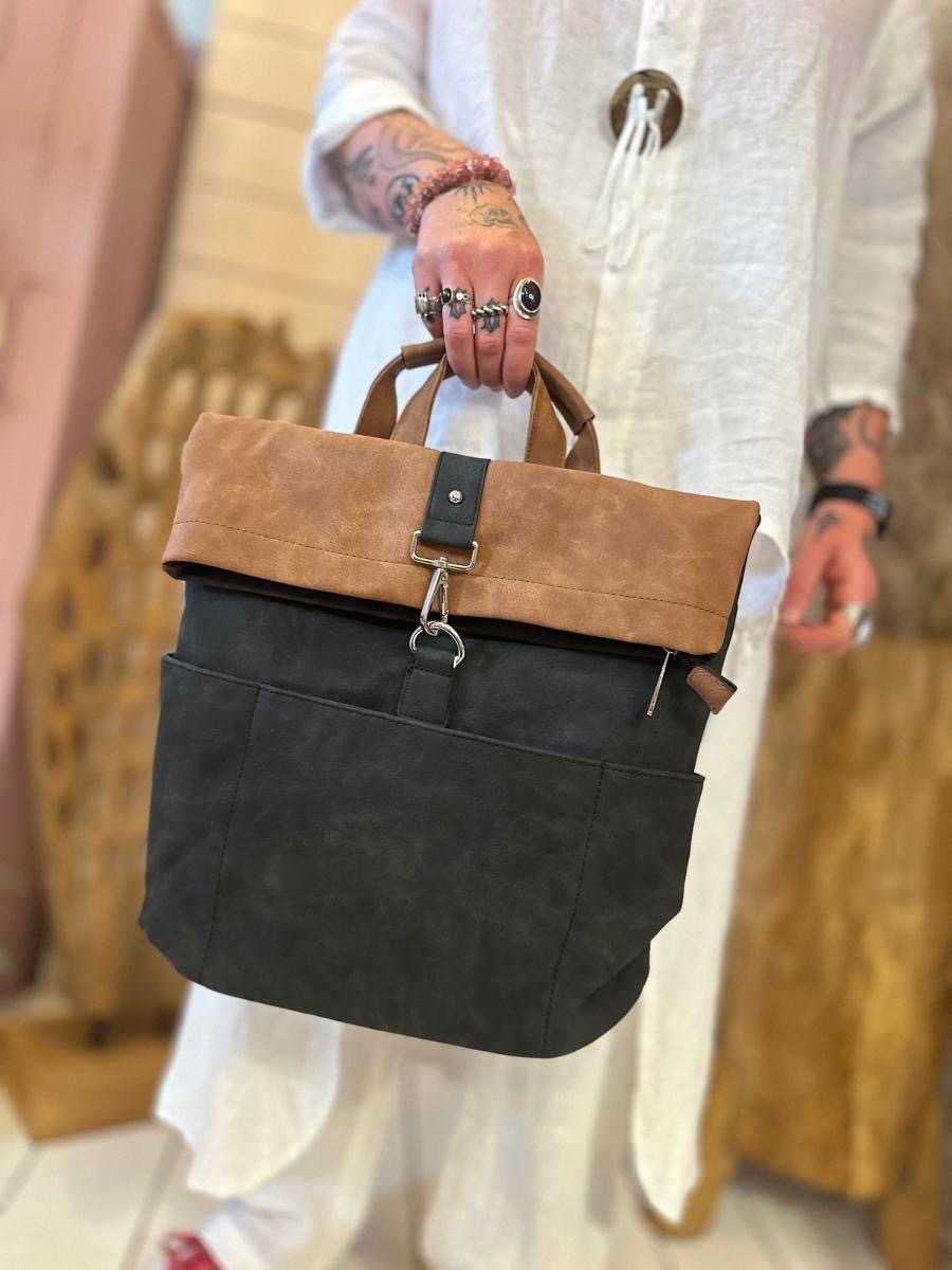 Person in a white outfit holding a two-tone brown and black tote bag with front pockets and a clasp fastening, standing indoors.