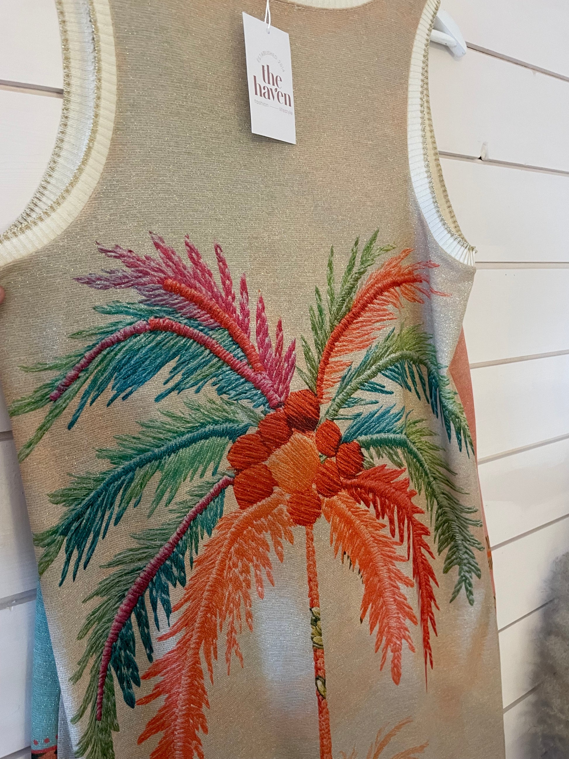 Sleeveless maxi dress featuring a colourful embroidered palm tree design, made from vegan materials and shown on a hanger against a white wooden wall.