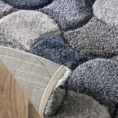 Close-up of a corner of a contemporary rug in various shades of grey and blue on a wooden floor, with the corner folded over to reveal the hardwearing polyester rug backing.