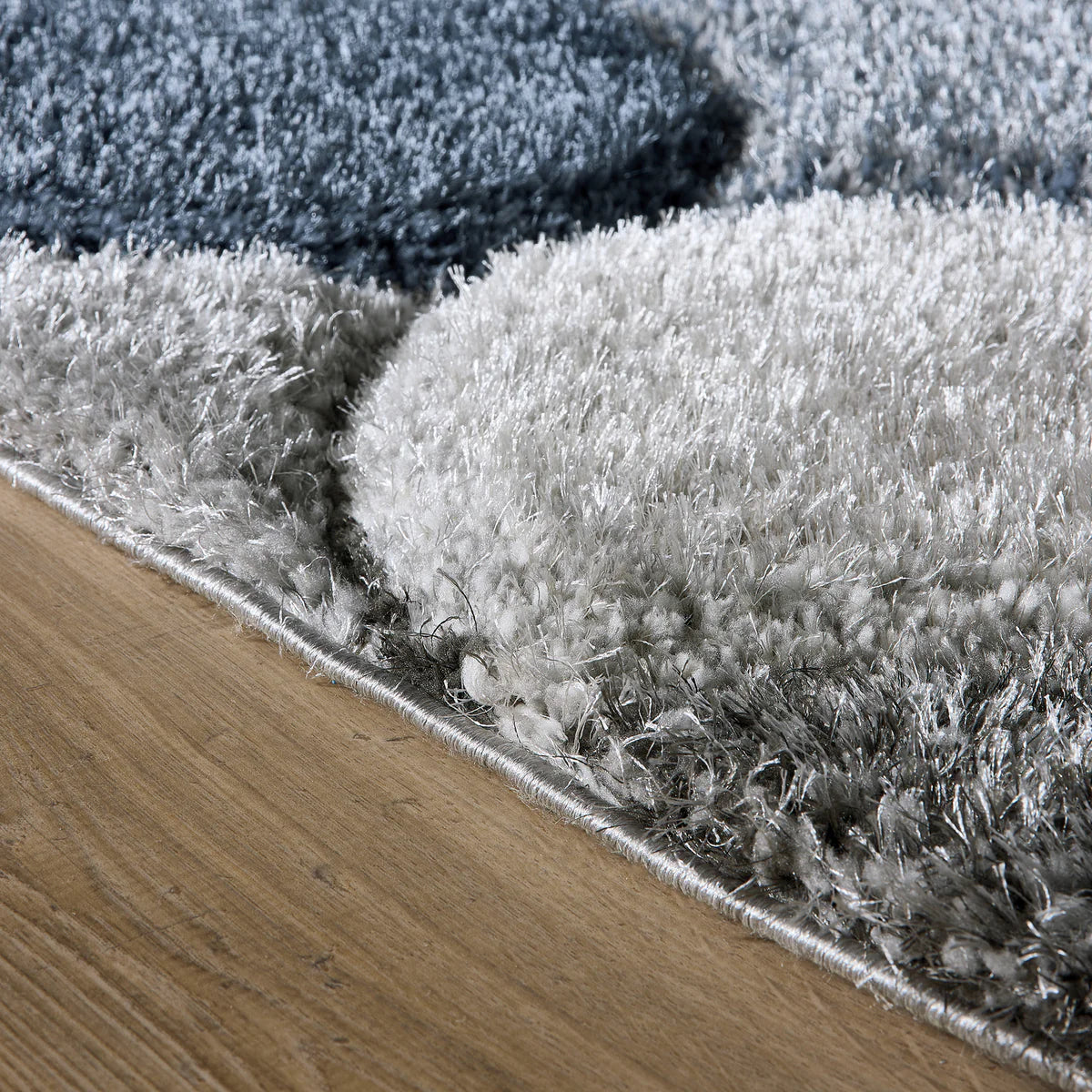 Close-up of a modern rug, the 3D Swirl Navy Rug, displaying raised circular patterns in grey and blue shades on a wooden floor. Made from hardwearing polyester for enduring style.