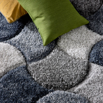 Two scatter cushions, one green and one mustard yellow, sit on a hardwearing polyester rug featuring overlapping grey, white, and blue circular patterns for a modern appearance.