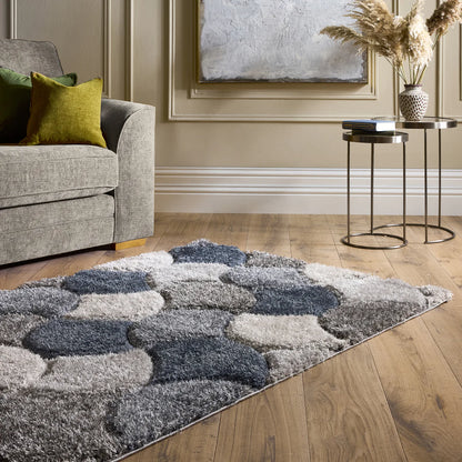 A modern living room features a 3D Swirl Navy Rug on wooden flooring, a grey sofa with green cushions, a round table, vase with pampas grass, and abstract wall art for a fresh contemporary feel.