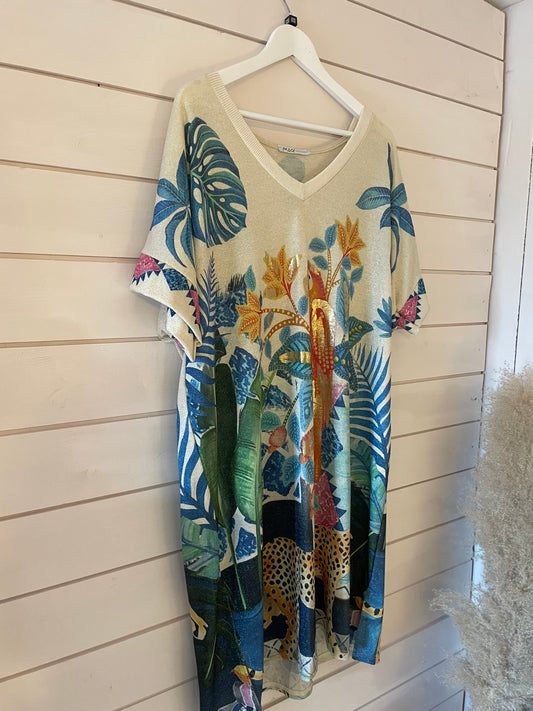 A short-sleeved, vegan-friendly dress with a V-neck hangs on a white hanger; it features a colourful tropical print with leaves, flowers and leopards.