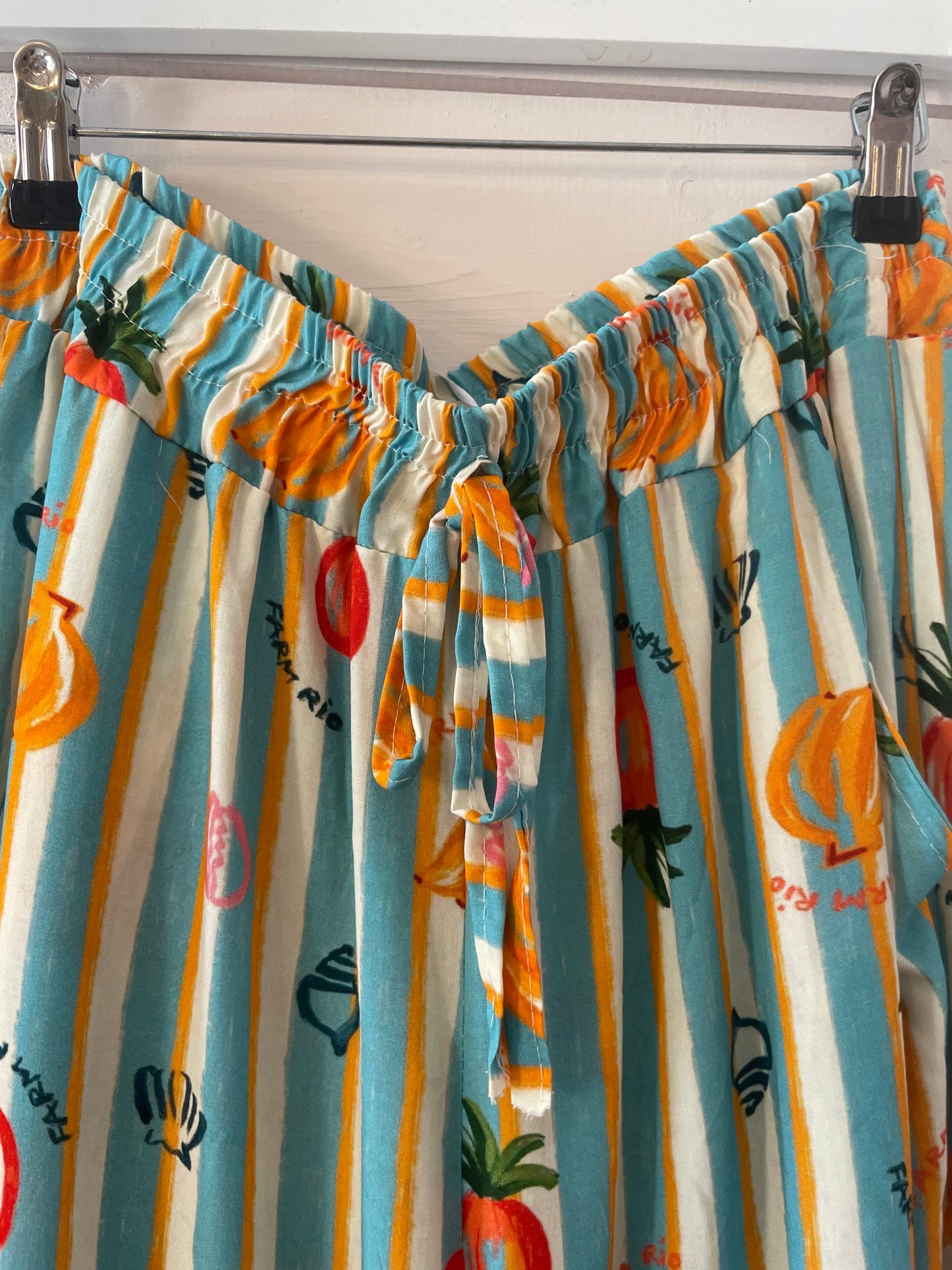 Colourful striped trousers with a fruit and vegetable print hang on clips. These lightweight trousers have an elasticated waistband, front fabric tie, and are made from vegan-friendly fabric for comfortable casual wear.