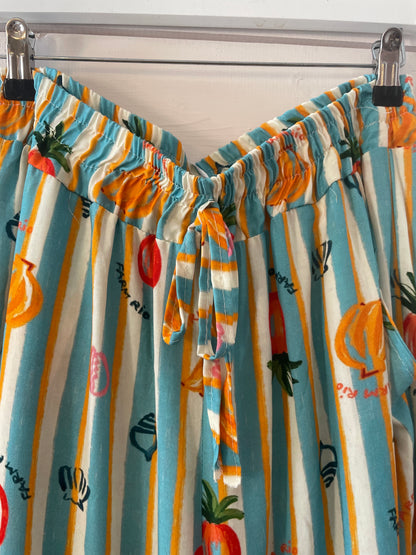 Colourful striped trousers with a fruit and vegetable print hang on clips. These lightweight trousers have an elasticated waistband, front fabric tie, and are made from vegan-friendly fabric for comfortable casual wear.