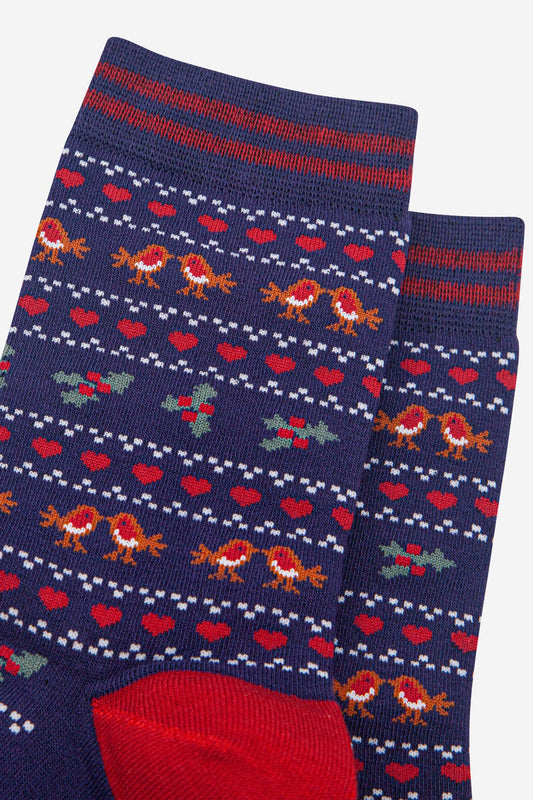 A pair of navy blue Christmas robin vegan socks with red heels, adorned with small red hearts, holly leaves and robins in a festive repeating pattern.