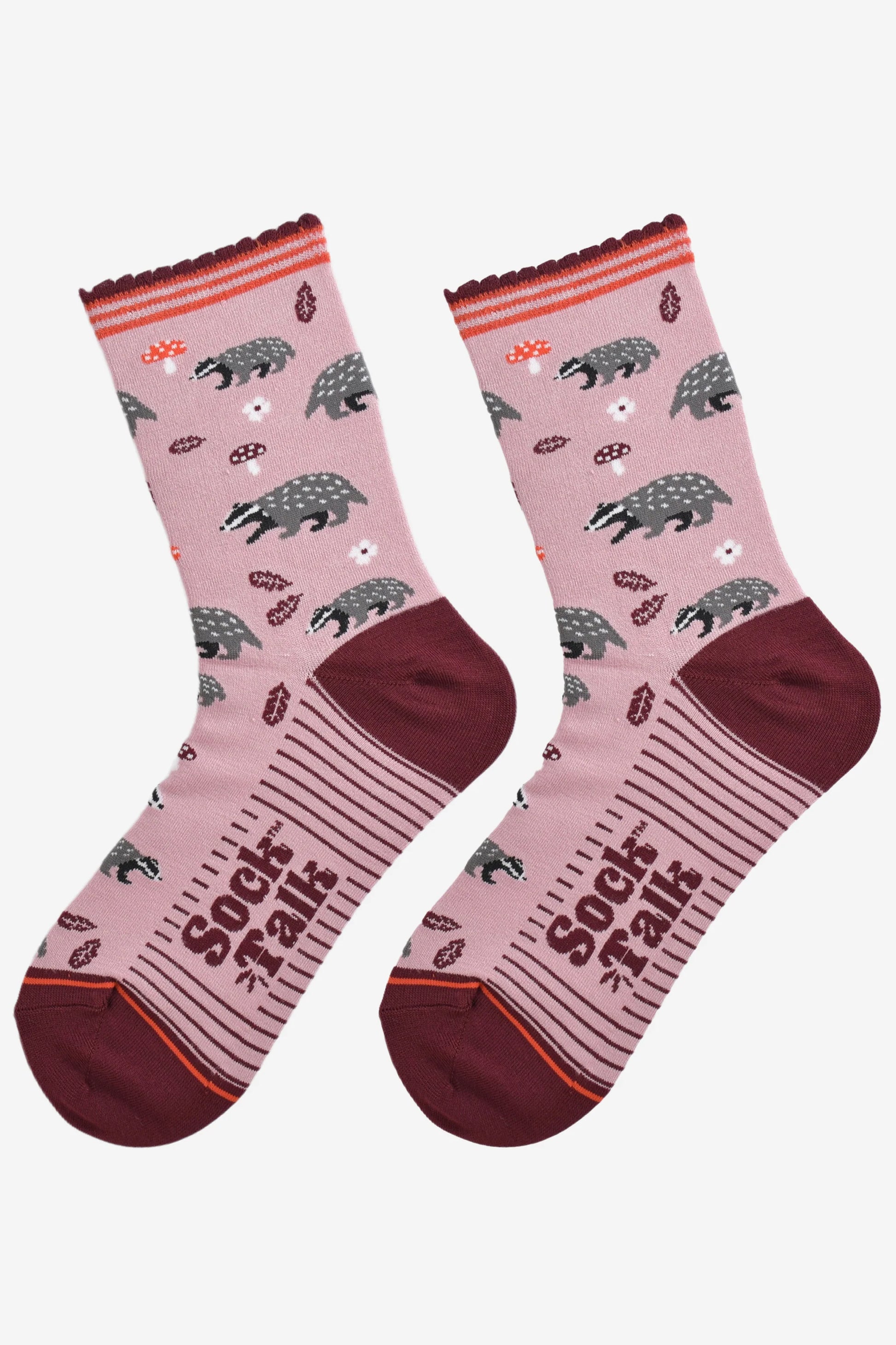 A pair of Vegan Badger Pink Socks with maroon heels and toes, decorated with anteater and ant motifs—cruelty-free socks for fans of playful, eco-friendly fashion. “Sock It to Me” is printed on the soles.