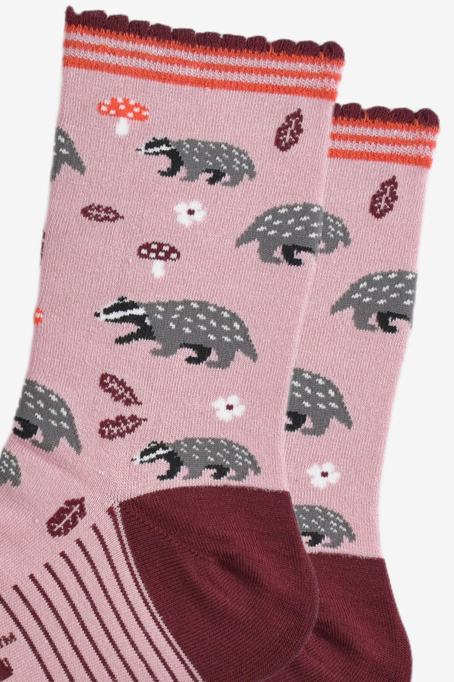A pair of Vegan Badger Pink Socks with maroon toes and cuffs, adorned with playful patterns of badgers, mushrooms, and leaves—cruelty-free socks ideal for eco-conscious fashion enthusiasts.