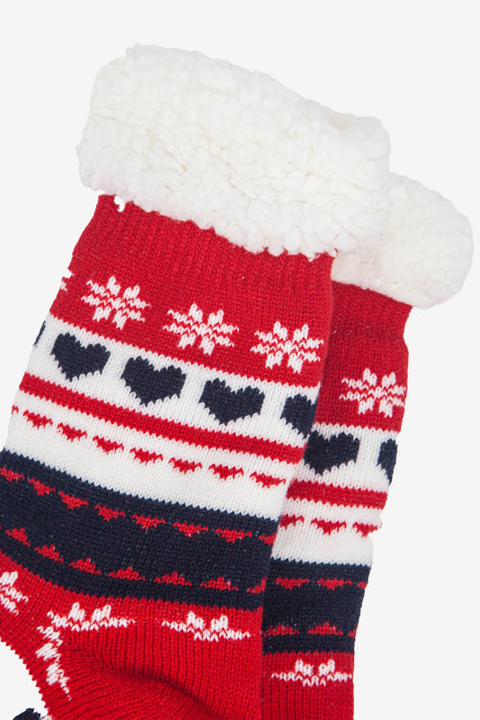 A pair of festive socks in red knit with white fluffy cuffs, adorned with heart and snowflake patterns in white and navy blue—perfect cosy vegan slipper socks for the season.