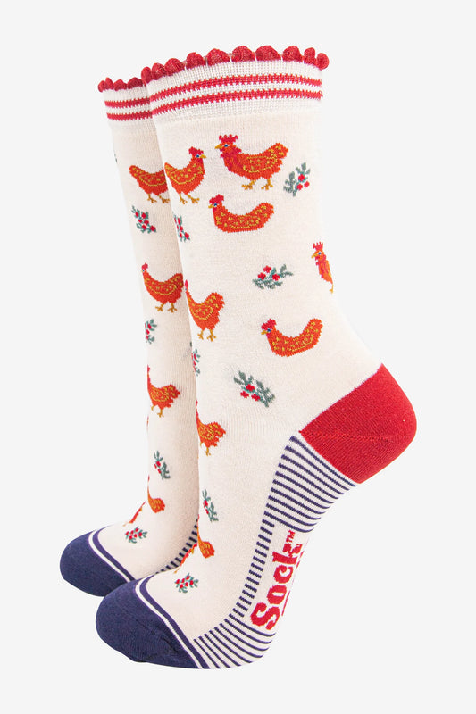 Pair of cream-coloured, animal-friendly socks featuring red chickens and floral designs, red scalloped tops, red heels, blue toes, and the word "Socks" in red on the sole.