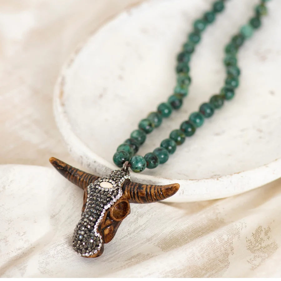 A beaded chain necklace featuring a carved buffalo head pendant embellished with small stones, gracefully presented on a round white dish.
