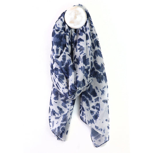 A recycled blend scarf with a blue and white pattern hangs loosely from a circular wall hook against a plain white background, combining style with an environmentally-friendly touch.