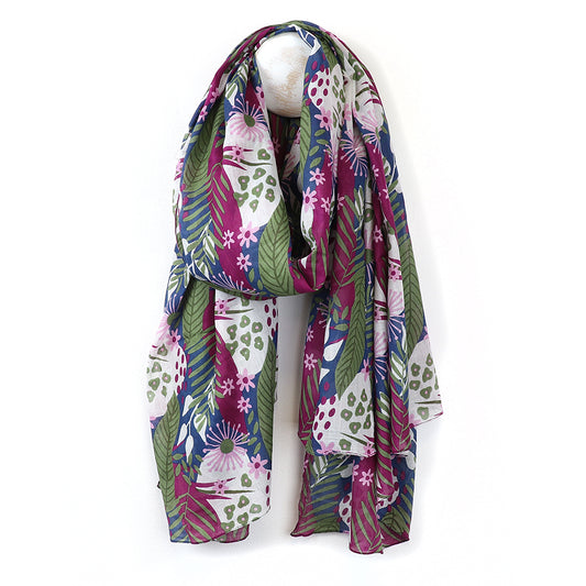 An opulent scarf featuring botanical prints with vibrant floral and leaf patterns in shades of purple, green, and white is elegantly displayed against a plain background.