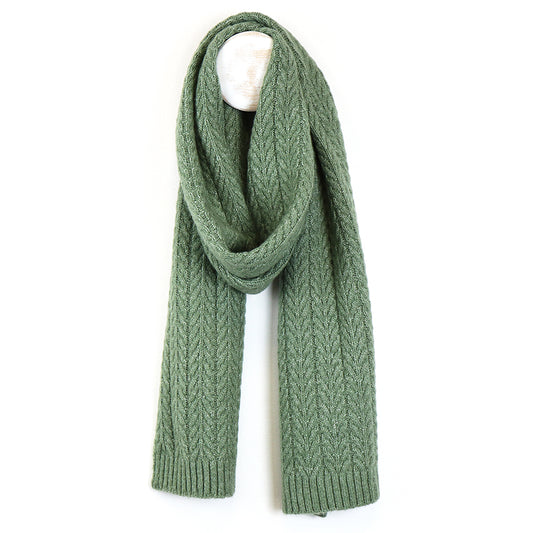 A sage scarf, made from recycled vegan yarn, displays a chevron pattern and hangs over a white hook against a simple background.
