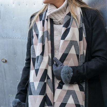 A person wearing a stylish chevron scarf, light polo-neck jumper, black coat, and gloves stands in front of a metal wall.
