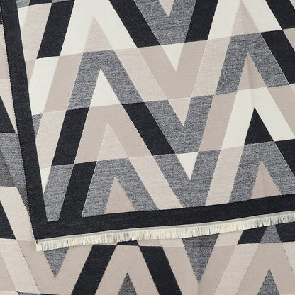 Geometric-patterned chevron scarf in tones of black, grey, and beige, displaying zigzag and triangle motifs with a visible fringe along one edge.