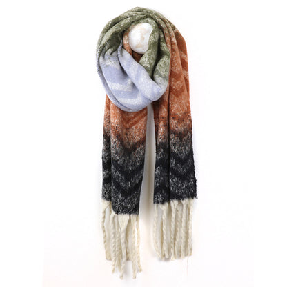 A long, fringed chevron scarf with a zigzag pattern in green, lavender, rust, black and cream colours hangs on a white hook.