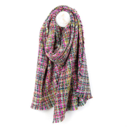 A multicoloured woven scarf with a fringed edge, made from vegan materials, is draped over a round white display stand against a plain white background.
