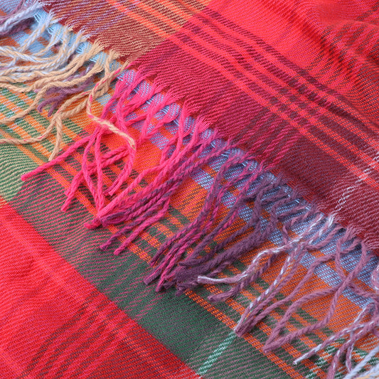 Close-up of a colourful accessory: a woollen plaid fabric with a tartan pattern and fringed edges in shades of red, pink, purple, and green.