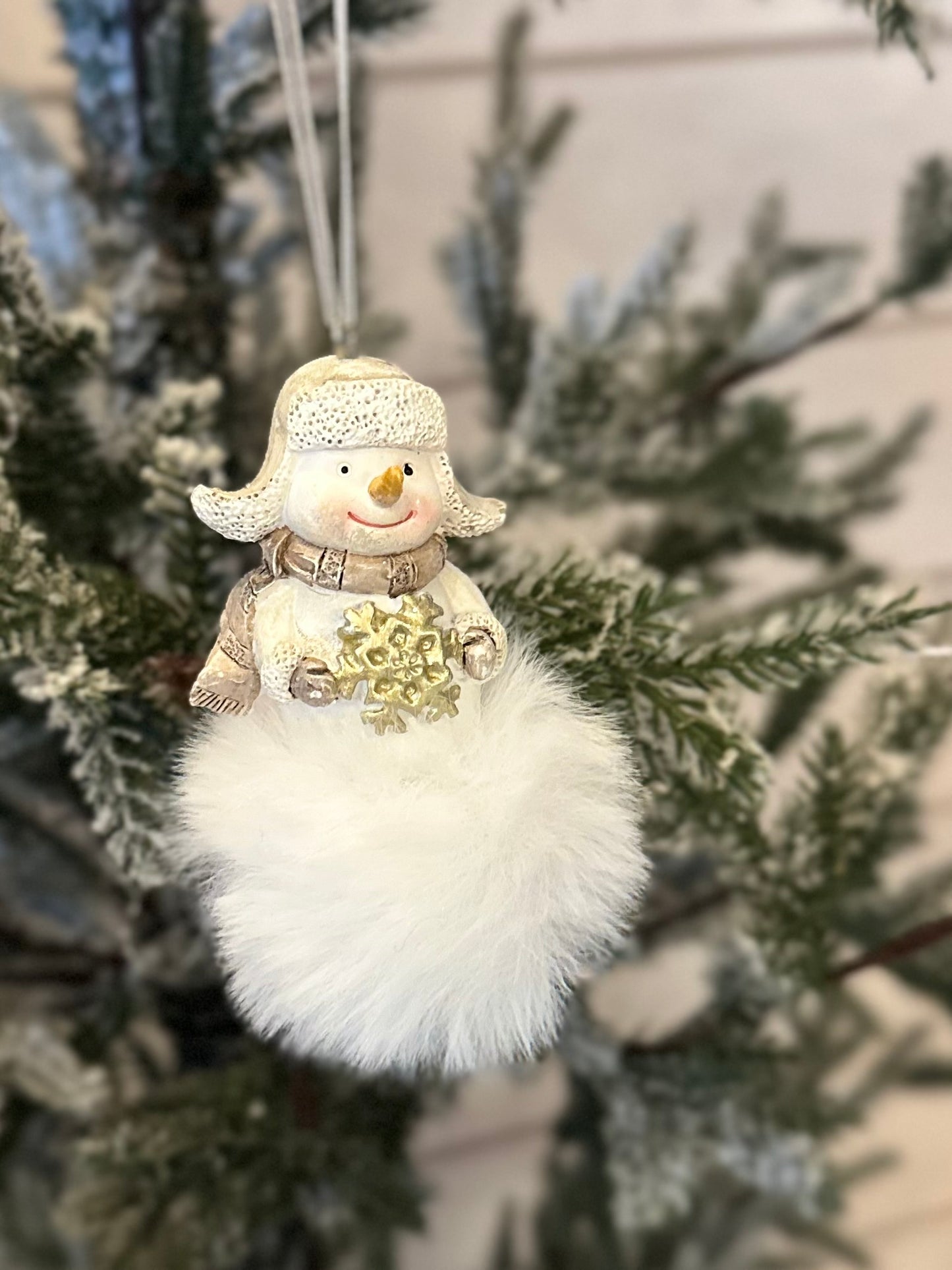 A handcrafted snowman decoration with a soft, fluffy white base hangs from a frosted Christmas tree branch, bringing charm to any festive display.