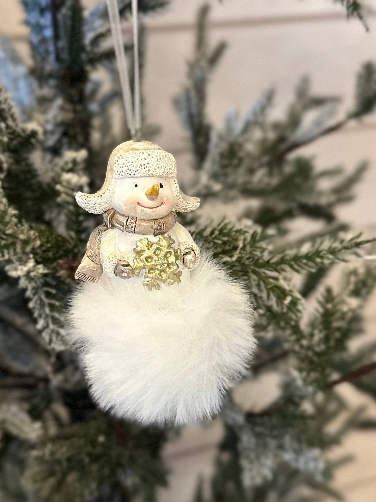 A handcrafted snowman decoration with a soft, fluffy white base hangs from a frosted Christmas tree branch, bringing charm to any festive display.