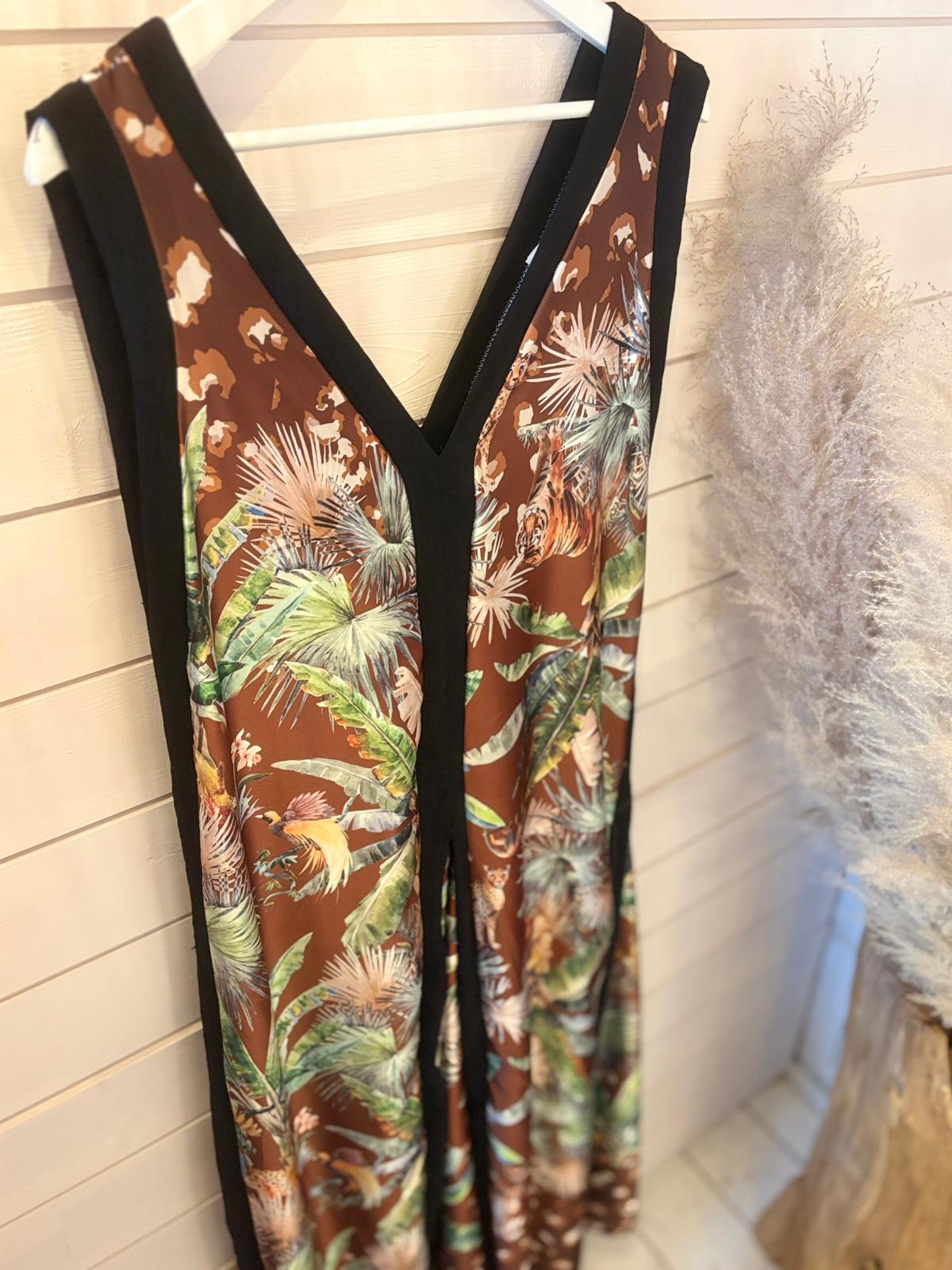 Sleeveless V-neck jungle jumpsuit dress with a brown tropical leaf print, black trim, and breathable fabric hangs on a white hanger next to a bundle of dried pampas grass.
