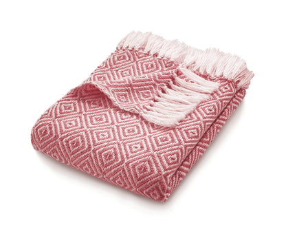 A folded pink and white patterned sustainable throw with fringe on one edge, made from recycled plastic bottles, displayed against a white background.