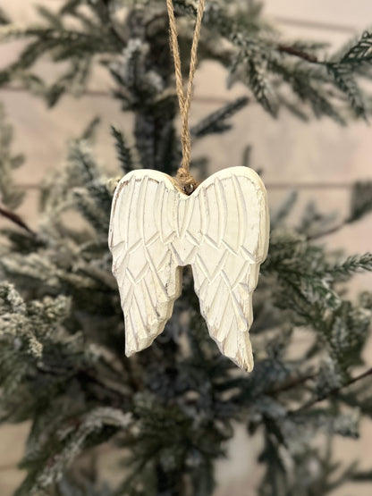 A white wooden angel wings ornament hangs from twine on a Christmas tree with green, frosted branches, bringing a charming touch to your festive décor.