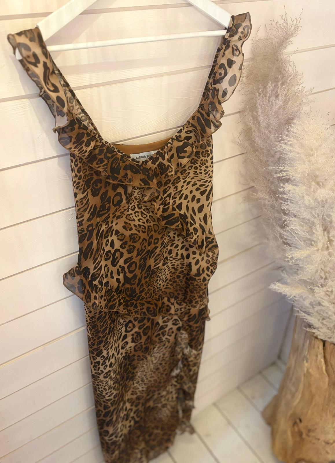 A sleeveless, ruffled Leopard Long Dress in size 12 is displayed on a white hanger against a wooden wall, with a pampas grass arrangement next to it.