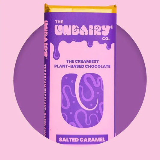 A purple and yellow salted caramel chocolate bar labelled “The UnDairy Co. Salted Caramel, The Creamiest Plant-Based Vegan Chocolate” on a pink background.