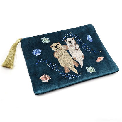 Dusky teal blue cotton velvet pouch with embroidered otters holding hands, surrounded by seashells. Finished with a metallic gold tassel on the zip.