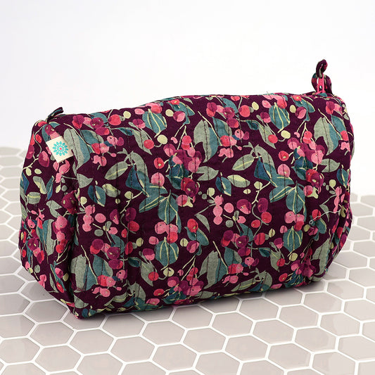The Winter Berry Quilted Make-up Bag boasts a maroon background with pink and green floral patterns, ideal for keeping your beauty essentials on a chic white hexagonal tiled surface.