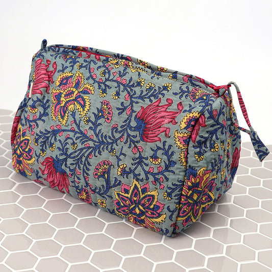 A blue paisley quilted make-up bag with colourful floral patterns sits on a white hexagonal tiled surface, bringing charm to your beauty essentials.