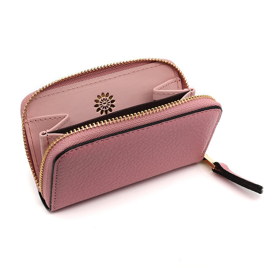 A pink zipped wallet with a gold zip, black trim, and an inner pocket showcasing a floral cut-out design—ideal to pair with your favourite travel make-up bag.
