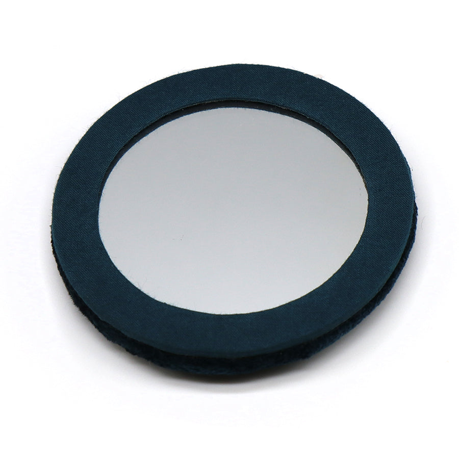 A round, flat embroidered mirror with a dark blue fabric border, set on a white surface—ideal as a travel mirror for stylish touch-ups while out and about.