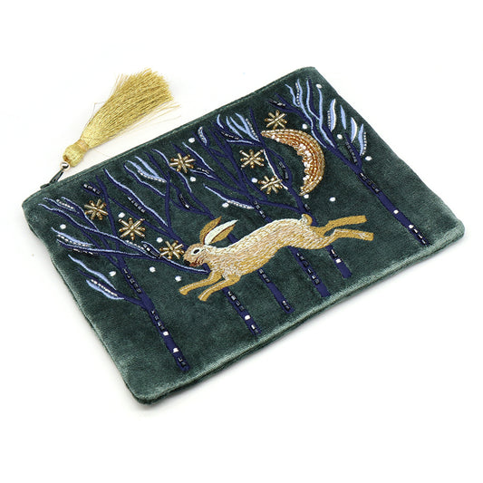 Green velvet zip purse embellished with an embroidered running hare, trees, and stars, featuring a gold tassel zip pull—a luxurious accessory for nature enthusiasts.