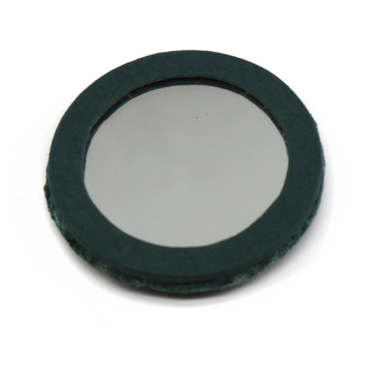 A round glass compact mirror with a dark green or black border, resting flat on a white surface, evocative of a refined velvet-embroidered accessory.