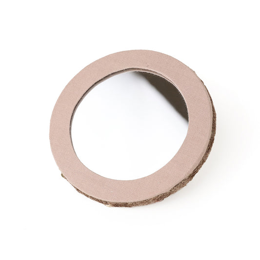 A round compact mirror with a beige fabric frame and partially brown textured backing, set against a white background.