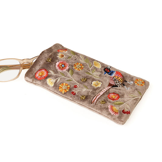 A pair of spectacles partially tucked into a beige velvet glasses case decorated with embroidered flowers and a bird.